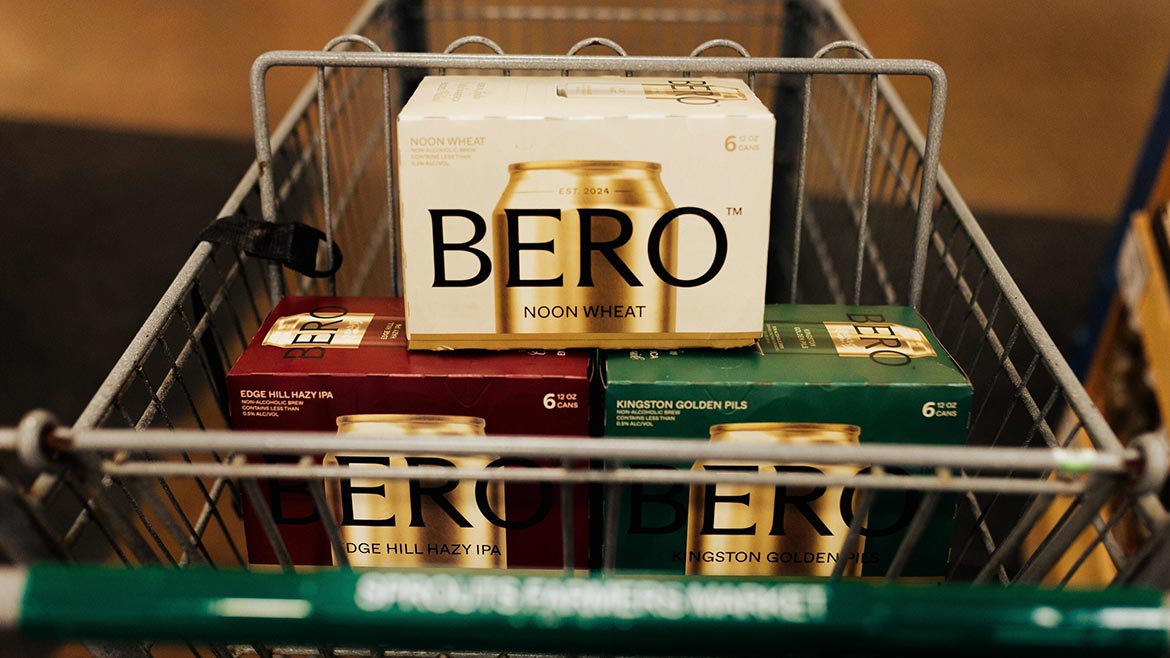 Shopping cart containing non-alcoholic beer variety packs in multiple styles, including wheat, hazy IPA, and pilsner.