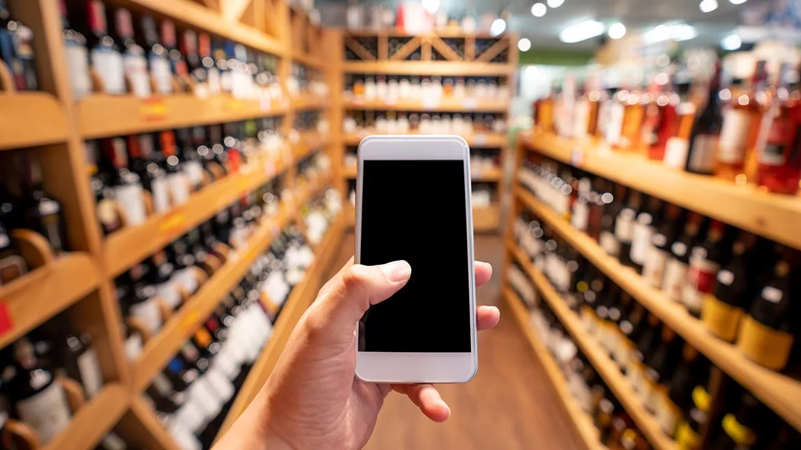 man holding a phone in a wine aisle