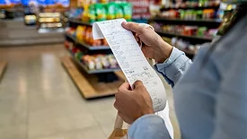 a person reviewing a long thermal paper receipt in a grocery store.
