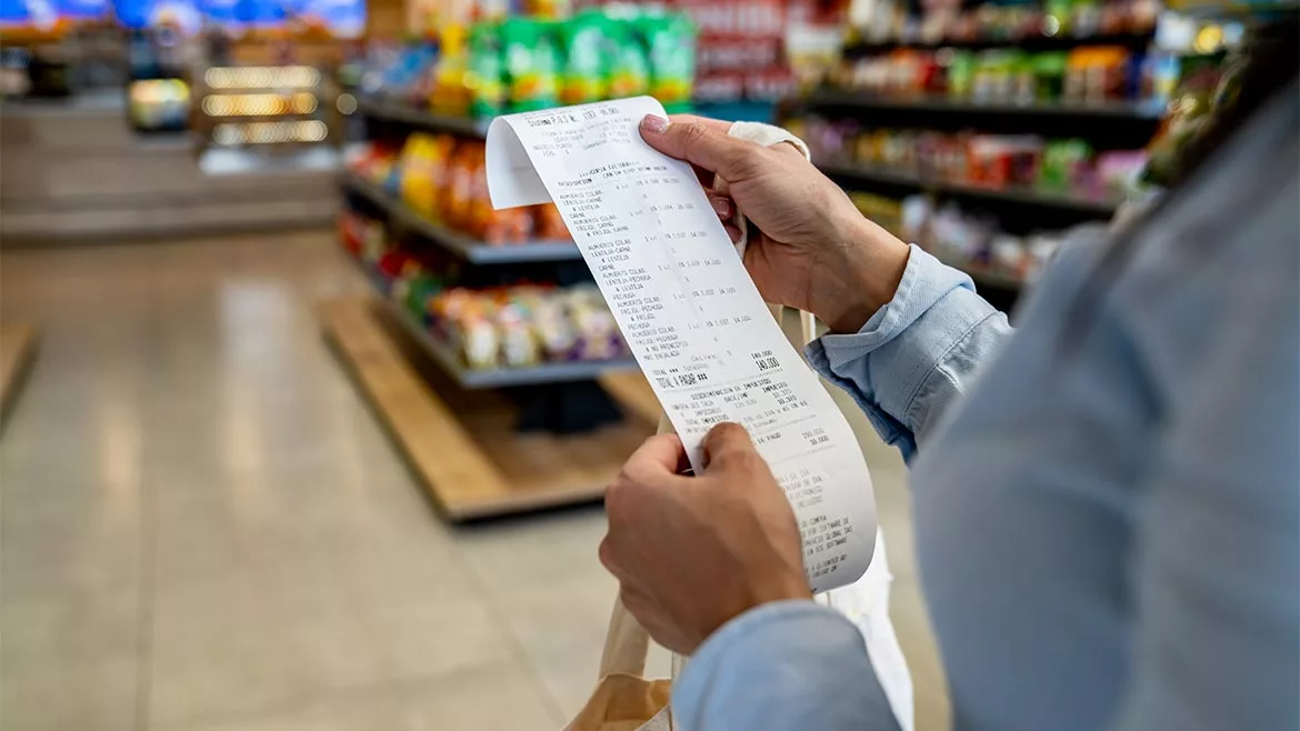 a person reviewing a long thermal paper receipt in a grocery store.