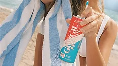 a person holding a can of Gorgie Protein Energy Drink in the Rocket Pop flavor next to a blue-and-white striped beach towel