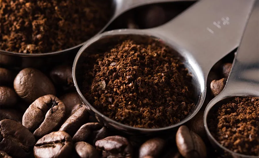 medium-to-dark roasted coffee beans alongside metal scoops filled with finely ground coffee medium-to-dark roasted coffee beans alongside metal scoops filled with finely ground coffee