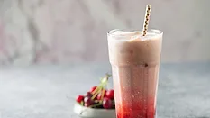 a cherry-flavored dirty soda served in a tall glass with a straw, accompanied by fresh cherries on the side
