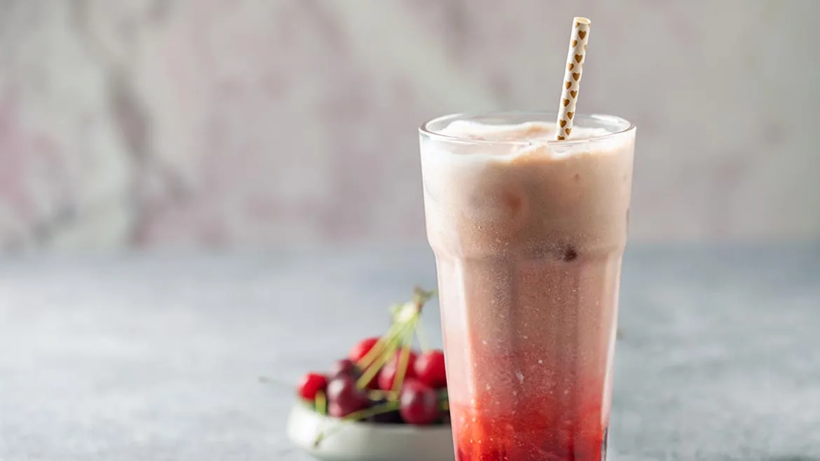 a cherry-flavored dirty soda served in a tall glass with a straw, accompanied by fresh cherries on the side