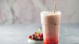 a cherry-flavored dirty soda served in a tall glass with a straw, accompanied by fresh cherries on the side