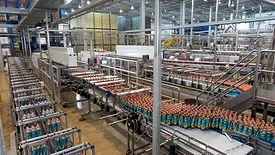 This image depicts a modern industrial bottling plant, likely for beverages, utilizing automated conveyor systems to transport products. 