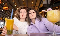 This image shows two people making a funny face while holding drinks in a restaurant or cafe setting