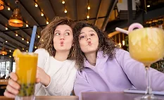 This image shows two people making a funny face while holding drinks in a restaurant or cafe setting