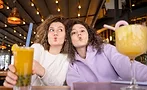 This image shows two people making a funny face while holding drinks in a restaurant or cafe setting