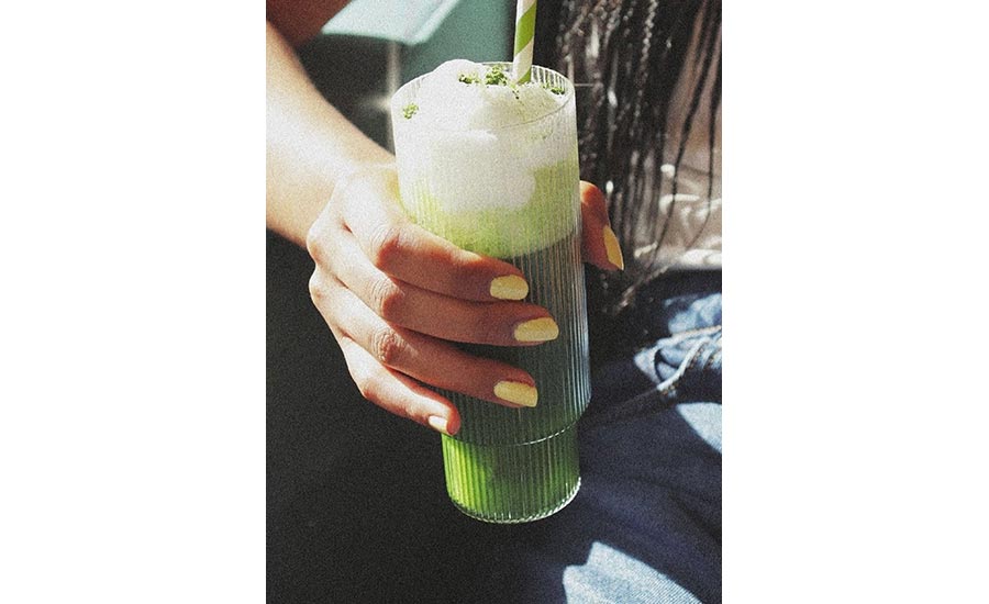  a vibrant green iced matcha latte layered with milk in a tall, ribbed glass tumbler