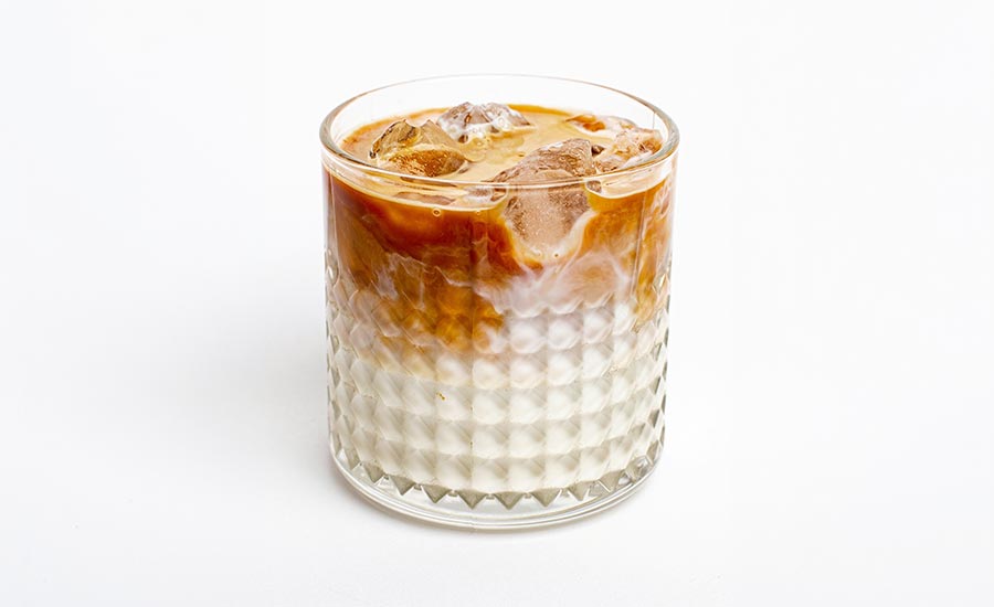 an iced latte served in a textured glass tumbler with ice cubes and distinct layers of espresso and milk