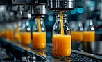  a food and beverage production facility with glass bottles being filled with orange juice on a conveyor belt