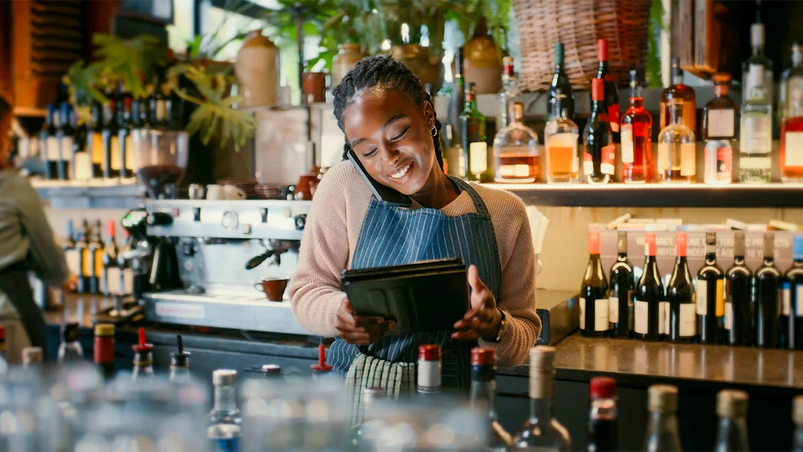 The image depicts a moment in time of a restaurant employee using technology to manage customer orders and service. 