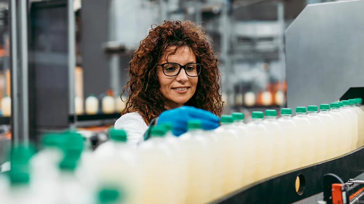 a quality control worker inspecting bottled beverages on an automated production conveyor line in a food and beverage manufacturing plant
