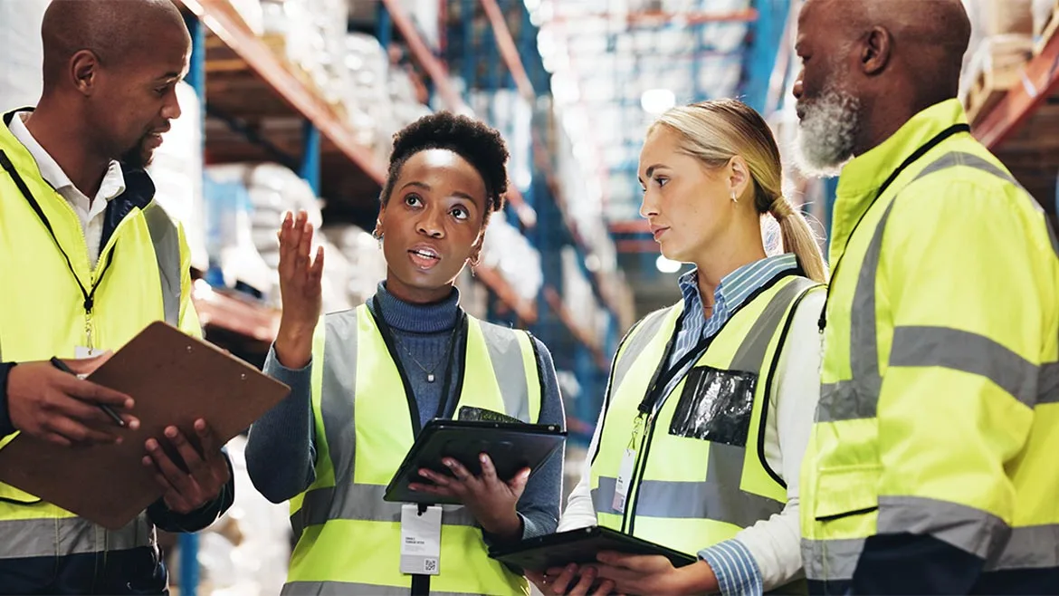 a diverse group of warehouse and supply chain professionals in high-visibility safety vests discussing logistics operations and digital data management a diverse group of warehouse and supply chain professionals in high-visibility safety vests discussing logistics operations and digital data management