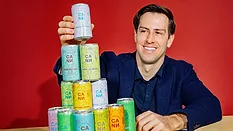 Jake Bullock, the co-founder and chief executive officer of the THC-infused social tonic brand Cann, posing alongside a stacked pyramid of various Cann beverage cans Jake Bullock, the co-founder and chief executive officer of the THC-infused social tonic brand Cann, posing alongside a stacked pyramid of various Cann beverage cans