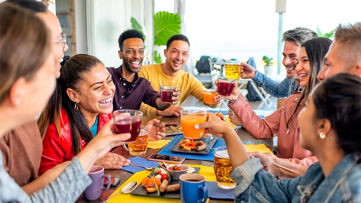 a diverse group of happy friends gathered around a table indoors, sharing a meal and drinks
