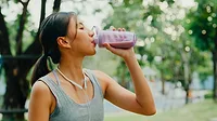 a person drinking a purple beverage from a shaker bottle outdoors near trees a person drinking a purple beverage from a shaker bottle outdoors near trees