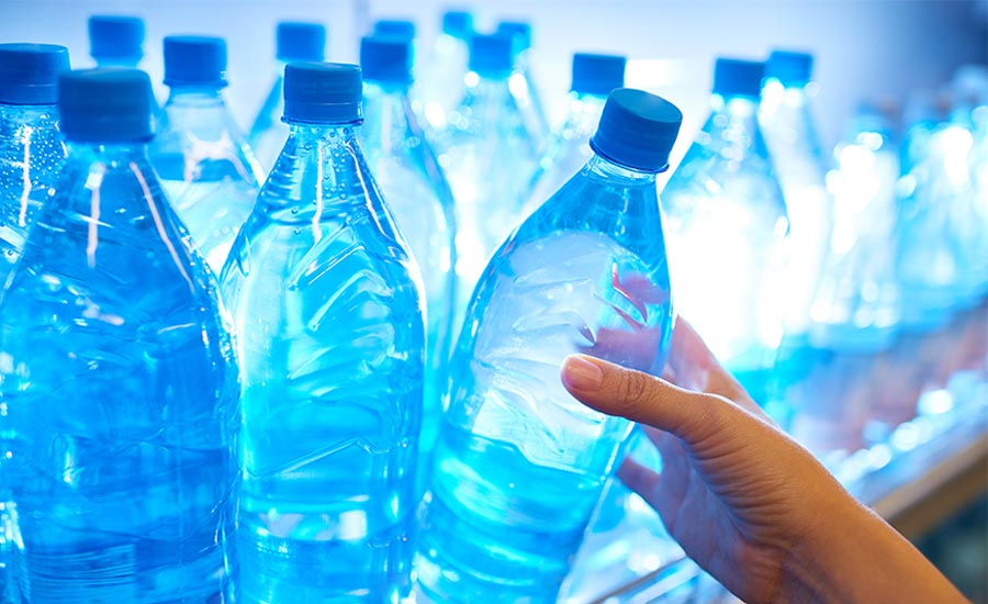  a hand reaching for a clear plastic water bottle with a blue cap on a refrigerated store shelf