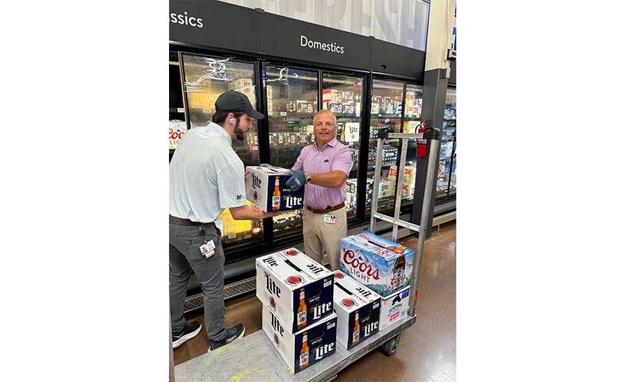 a delivery worker and a store employee stocking Miller Lite and Coors Light beer cases in a grocery store aisle