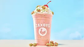 a pink Zaxby's cup with a handcrafted milkshake topped with whipped cream, colorful candy pieces, and a cherry