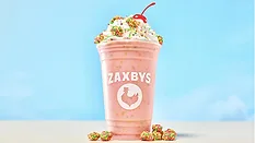 a pink Zaxby's cup with a handcrafted milkshake topped with whipped cream, colorful candy pieces, and a cherry