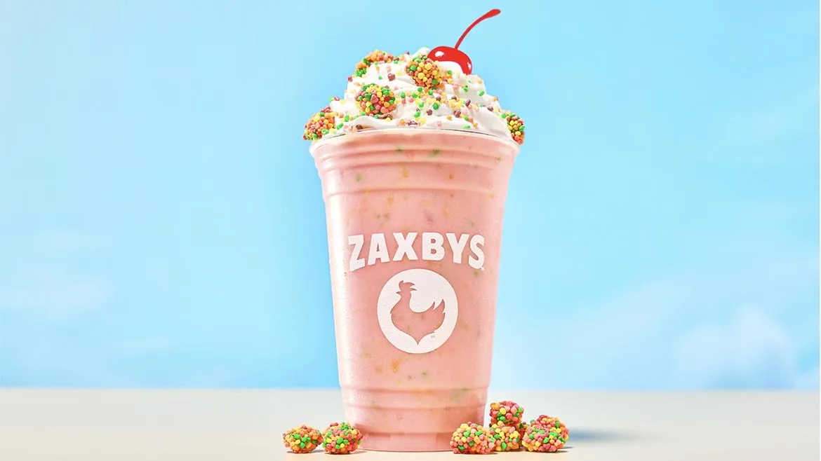 a pink Zaxby's cup with a handcrafted milkshake topped with whipped cream, colorful candy pieces, and a cherry