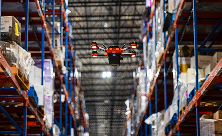 a Corvus One autonomous inventory drone from Corvus Robotics flying down a high-bay warehouse aisle to scan pallet locations