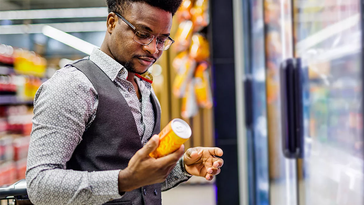 This image shows a man examining the label of a canned beverage in a store.